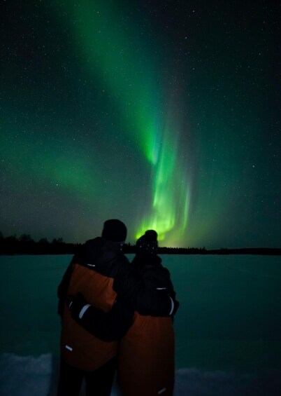 Two people observing the Northern Lights over a frozen landscape. 5