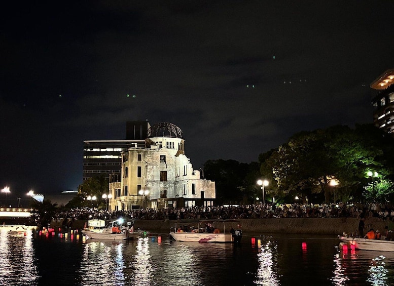 A historic building with a dome, illuminated by artificial lights, surrounded by a crowd of people and boats on the water. 4