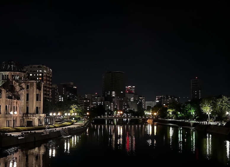 A nighttime cityscape with a river reflecting lights, modern buildings, and a statue. 1