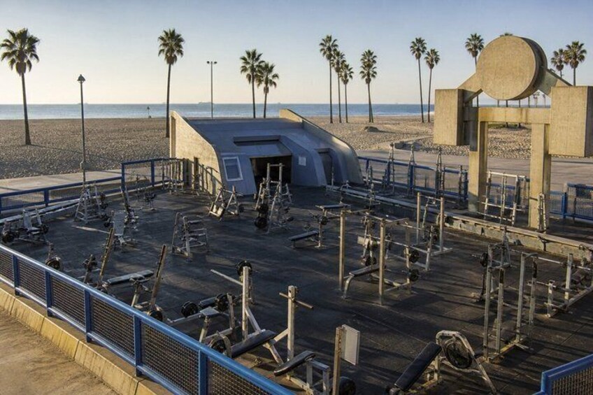A beach with exercise equipment, palm trees, and a concrete structure. 3