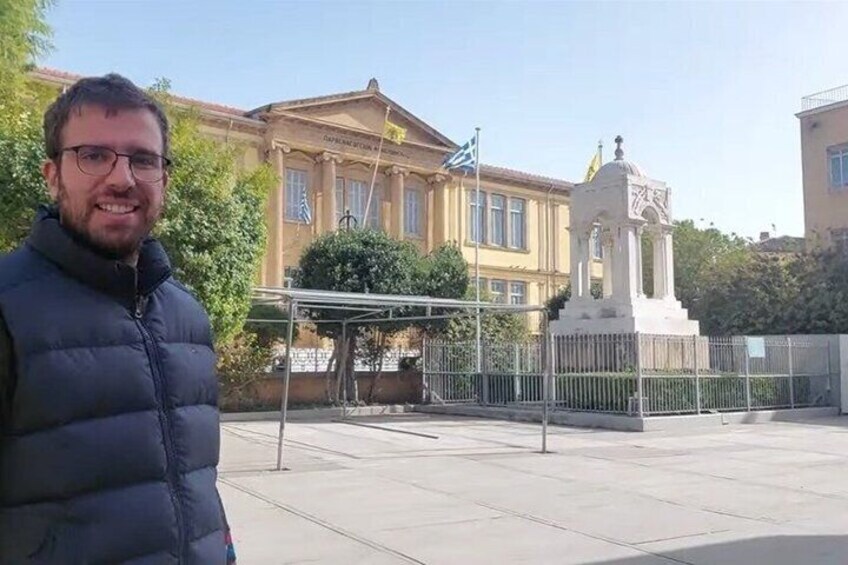 A man standing in front of a building with a white monument and a covered structure. 2