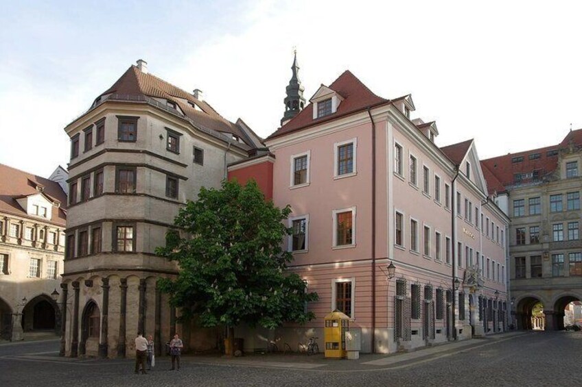 A cobblestone street with historic buildings, a large tree, and a yellow post box. 5
