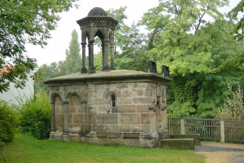 A stone structure with a dome and a bell tower, surrounded by greenery. 4