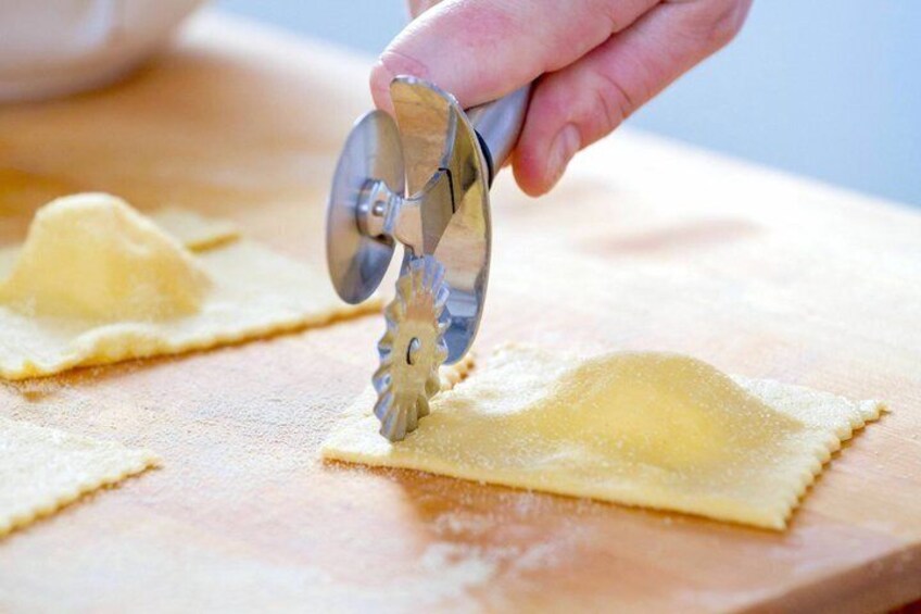 A hand using a pasta cutter on a wooden surface. 5