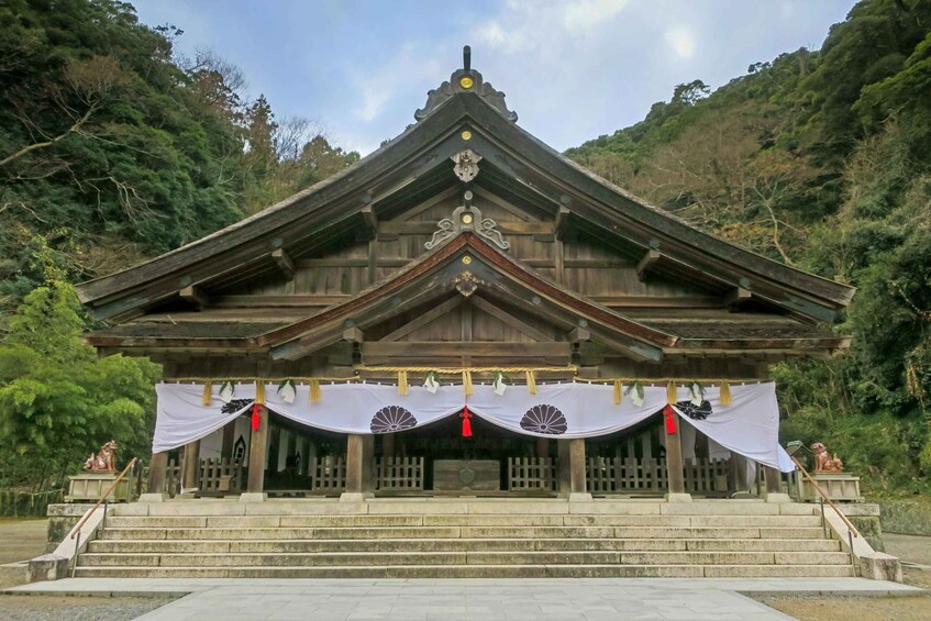 A traditional wooden shrine with a tiled roof, surrounded by lush greenery. 1