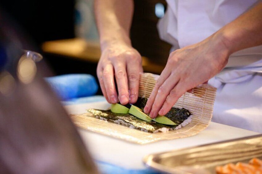 A person preparing sushi with rice and seaweed on a cutting board. 2