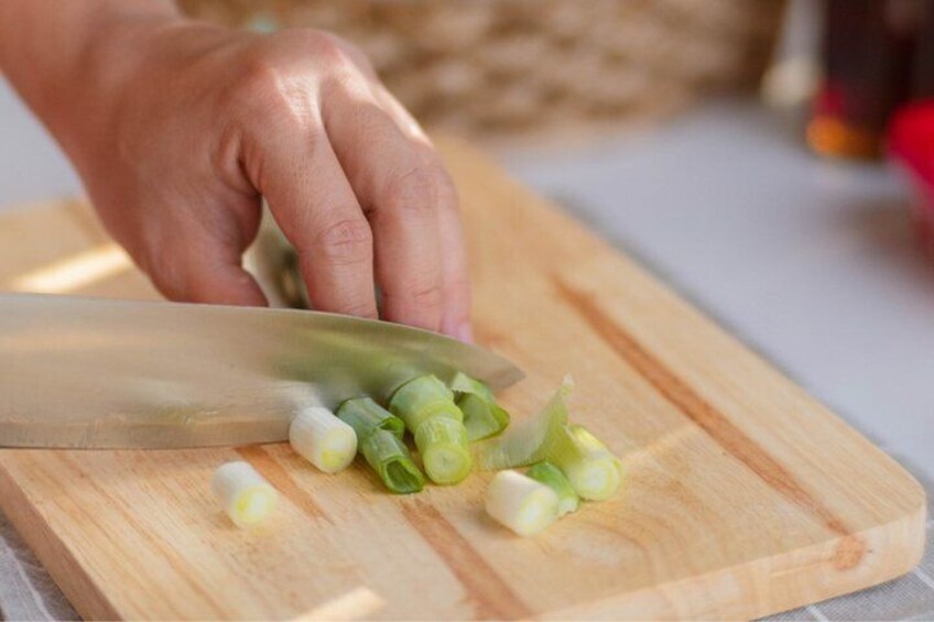 A hand chopping green onions on a wooden cutting board. 4