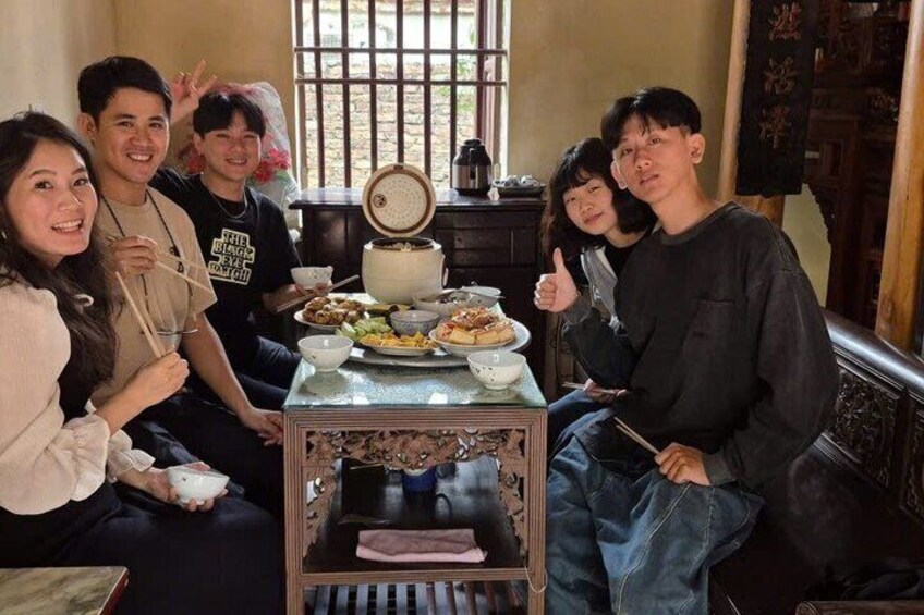 A group of people sitting around a table with food and drinks, a traditional clock, and a window with bars. 4