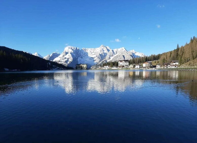 A calm lake with a reflection of snow-capped mountains and a small town with buildings along the shore. 2