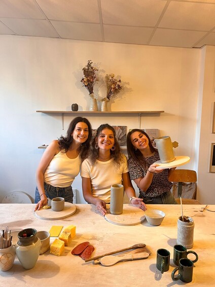 Three people in a pottery workshop with clay mugs and tools on the table. 2