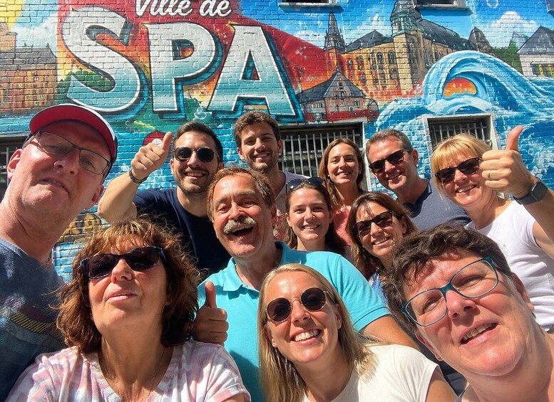 A group of people in front of a colorful mural with the text 'Ville de SPA'. 2