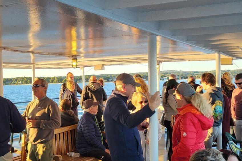 A group of people on a boat with a covered deck, a body of water, and a distant shoreline in the background. 4