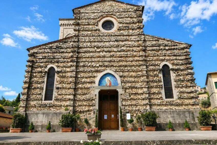 A stone church with a central arched doorway, flanked by two tall windows, and a circular window above the entrance. 4