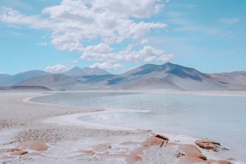 A salt flat with a curved shoreline, mountains in the background, and a clear sky. 1