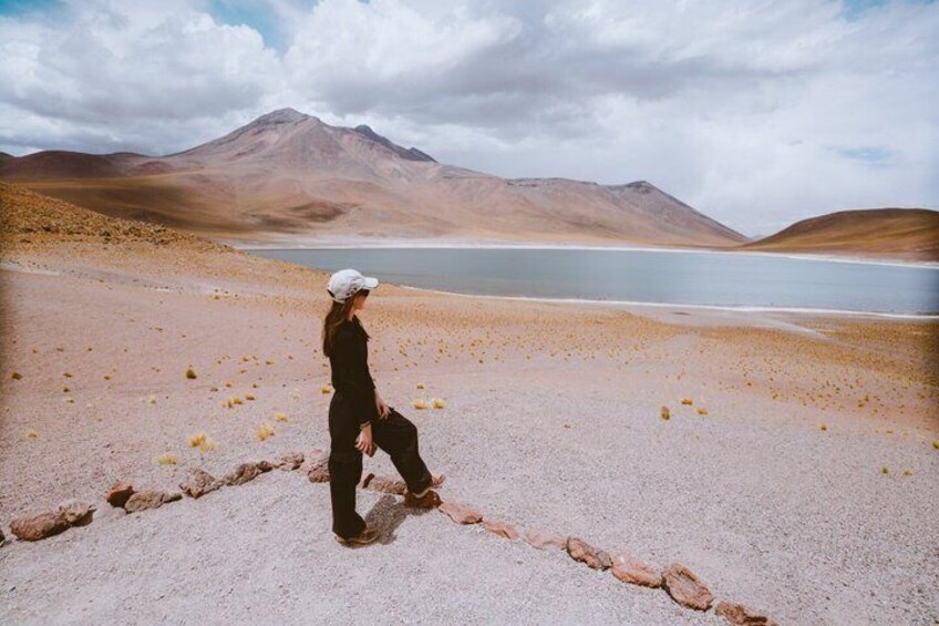 A person standing on a rocky terrain with a lake and mountains in the background. 2