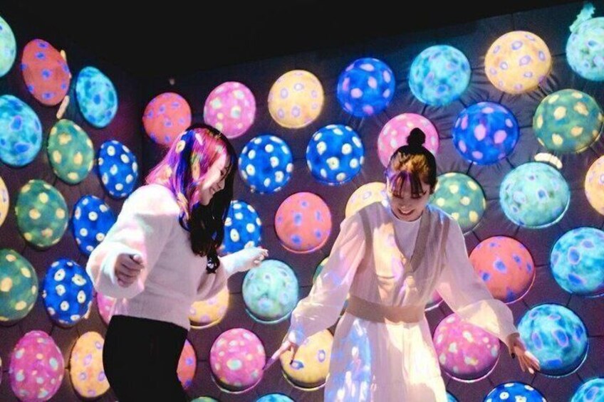 Two people in white outfits dancing in front of a wall of colorful spherical decorations. 2