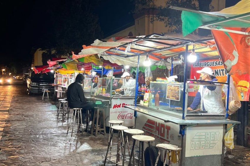 A street food stall with a Coca-Cola sign, a person sitting at a table, and a sign for 'Hamburguesas Nita'. 4