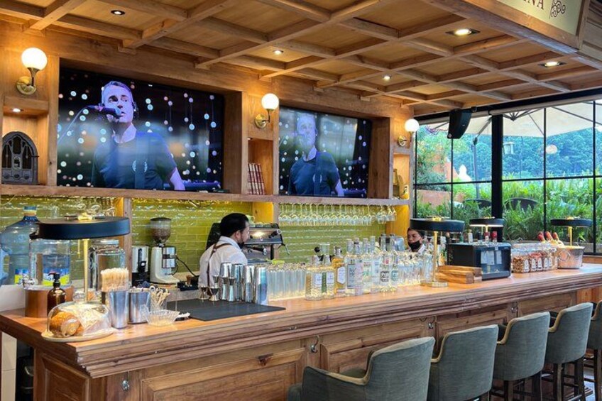 A bar with a wooden counter, bar stools, and a television screen displaying a person. 3