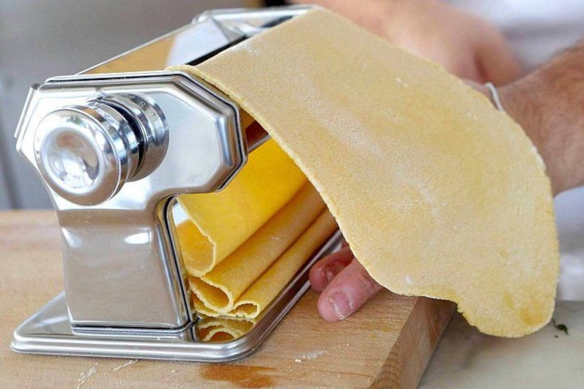 A person using a pasta machine to roll out dough. 2
