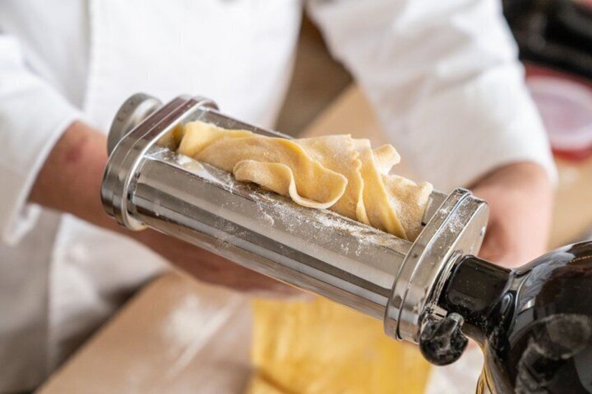 A person using a pasta machine to roll out dough. 4