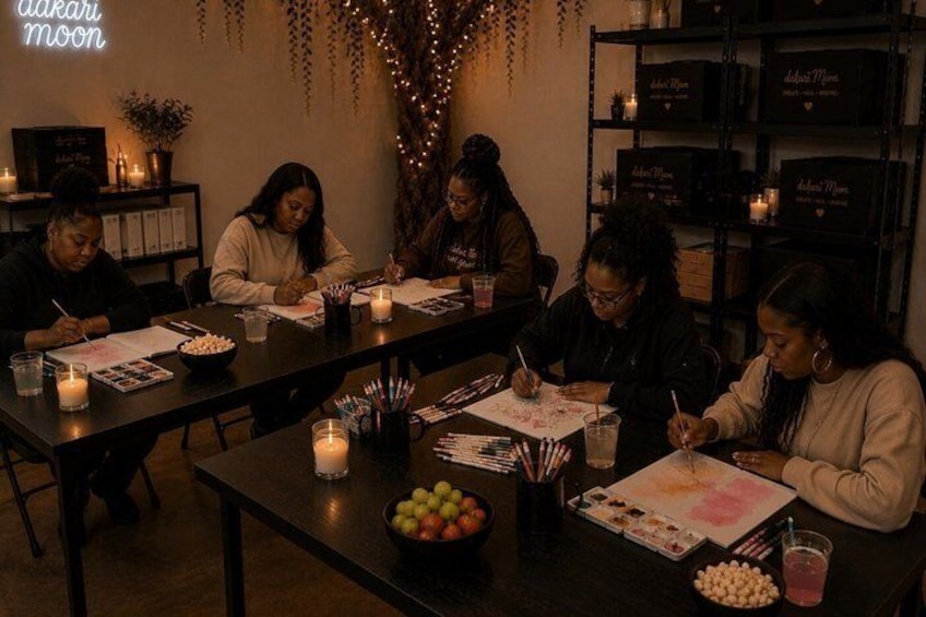 A group of people seated at a table, engaged in a drawing activity with art supplies. 2