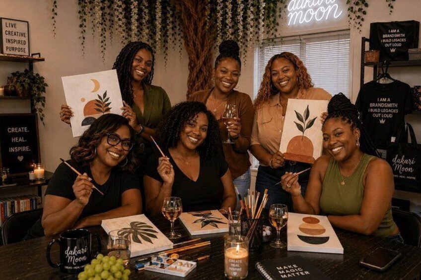 A group of people painting at a table with art supplies and canvases. 3