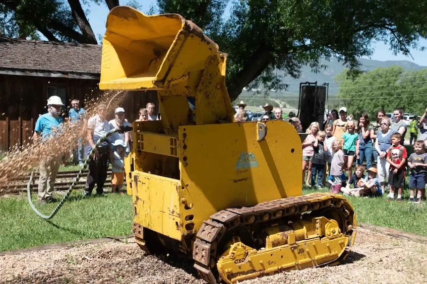 A yellow construction vehicle with a large bucket, surrounded by a crowd of people. 5