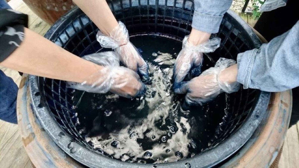 Hands wearing gloves mixing a dark liquid in a large container. 4