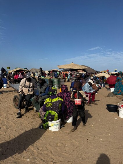 A busy outdoor market with people sitting and standing under umbrellas, and various goods displayed. 4