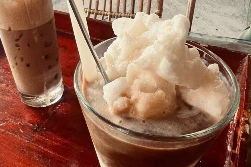 A glass of iced coffee with a spoon, next to a bowl of ice cream. 1