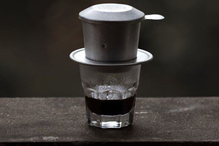 A clear glass with a metal filter on top, placed on a dark surface. 4