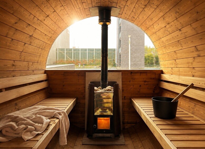 A sauna with wooden benches, a central heating unit, and a view of the outside. 3