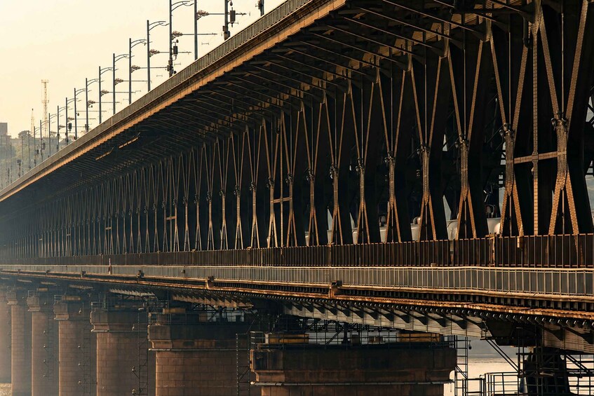 A large metal bridge with a complex truss structure, multiple support pillars, and a cityscape in the background. 5
