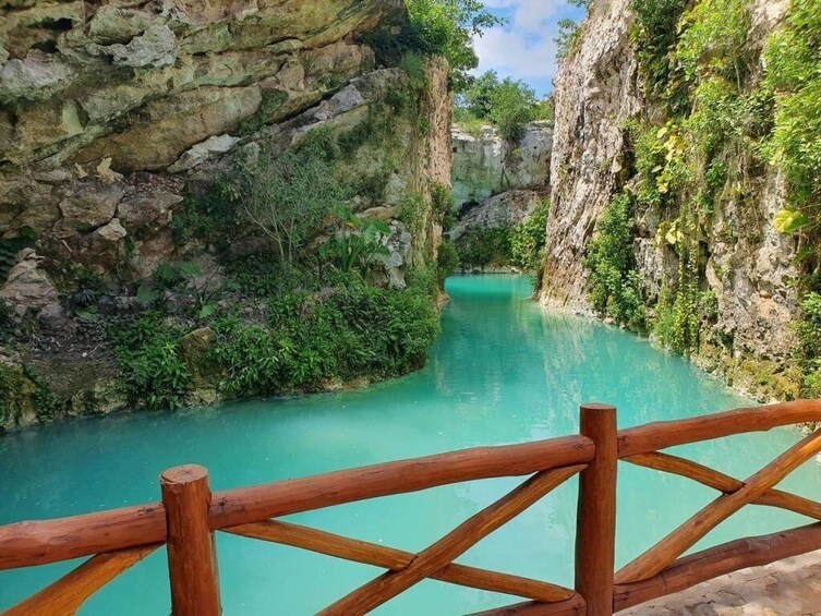 Ein türkisfarbener Fluss fließt durch eine felsige Schlucht. Im Vordergrund verläuft eine Holzlattenzaun. 1