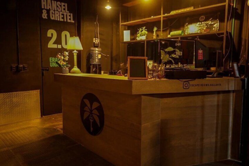 A reception desk with a logo, a lamp, and a shelf with items. 1