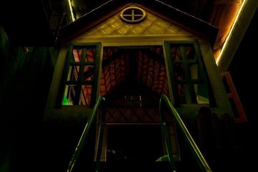 A dark, eerie house with a staircase leading up to a door with a cross symbol. 5