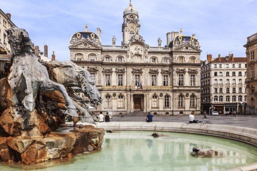 A historic building with ornate architecture, a fountain with a sculpture, and a clear sky. 3