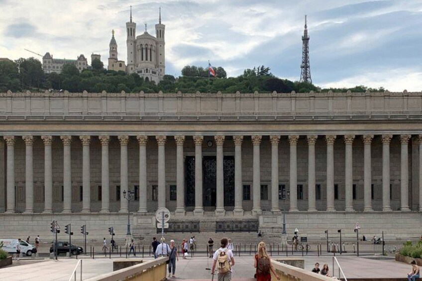 A large neoclassical building with columns, a fountain, and people walking around. 4