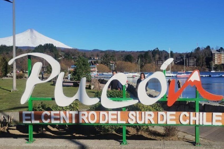 A sign with the text 'Pucon' and 'El Centro del Sur de Chile' against a backdrop of a mountain and a body of water. 3