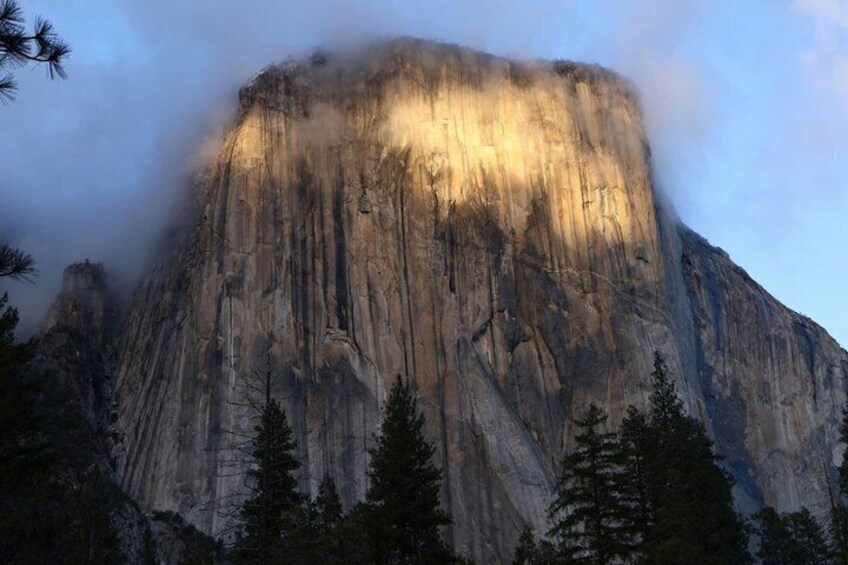 A mountain with a prominent face, surrounded by trees and clouds. 5