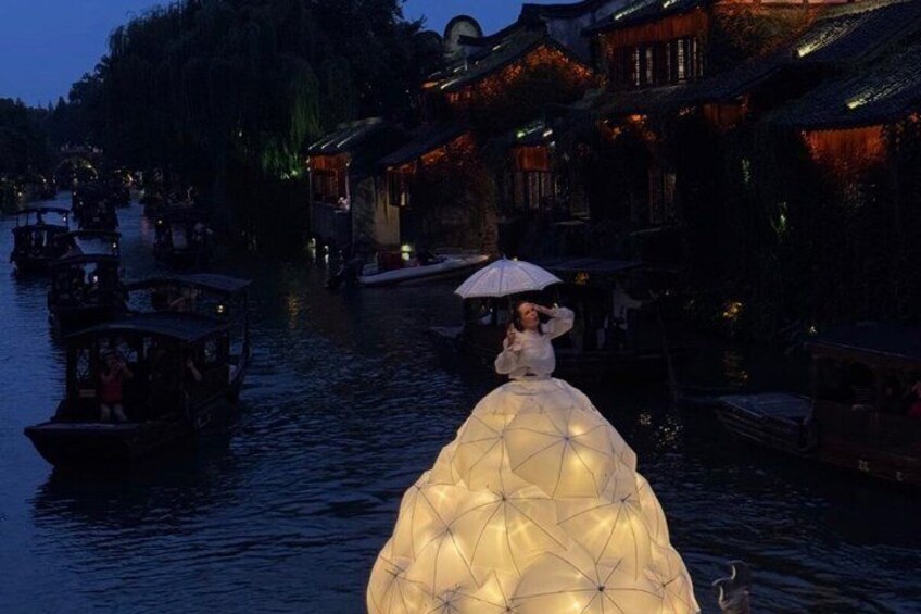 A traditional Chinese water village at dusk with illuminated buildings and boats on the water. 3
