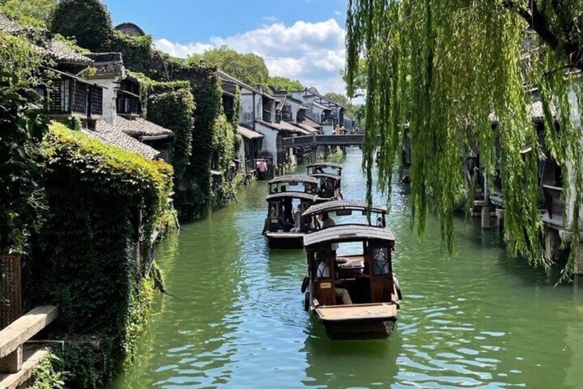 A narrow waterway with traditional boats, buildings with green ivy, and a bridge in the background. 2