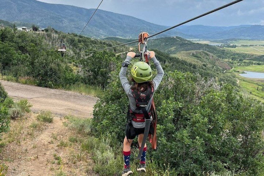 A person zip-lining over a mountainous landscape with greenery and a distant body of water. 3