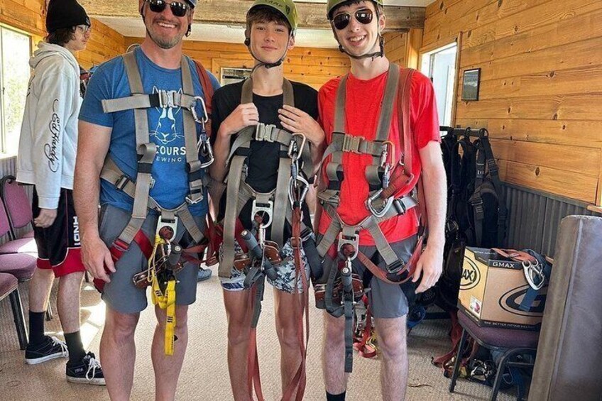 Four people wearing harnesses, standing in a room with wooden walls and a window. 5