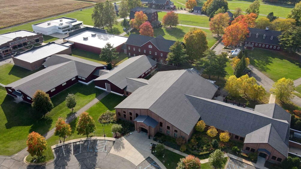 An aerial view of a campus with multiple buildings, green lawns, and trees with autumn foliage. 1