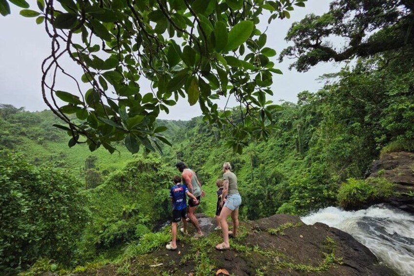 Two people standing on a rocky outcrop overlooking a waterfall in a lush, green forest. 5