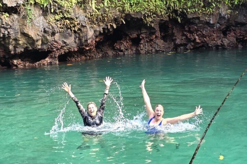 Two people swimming in clear water with their arms raised, surrounded by rocky cliffs. 1