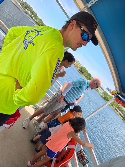 A group of people on a boat with life jackets, a man in a bright yellow shirt, and a clear view of the water and sky. 4