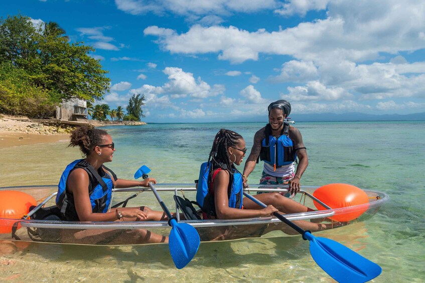 Three people in a kayak on a clear beach with turquoise water and palm trees in the background. 5
