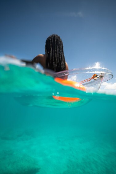 A person surfing with a transparent board, wearing a swimsuit, in clear turquoise water. 2